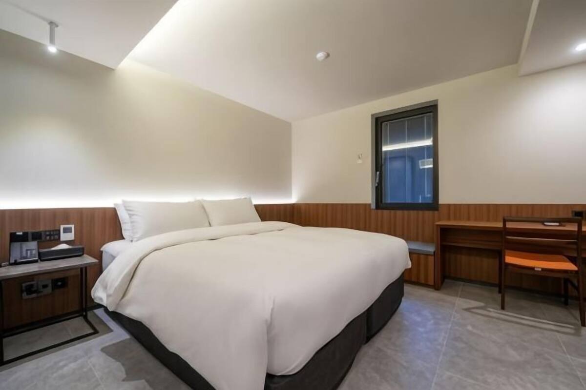 Una habitación de hotel con una cama grande, un escritorio, una silla, una mesita de noche y una ventana.