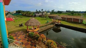 A view of a waterway with thatched-roof structures, a checkered area, and distant buildings. - CHUTI BEACH REOSORT (Mandarmani)