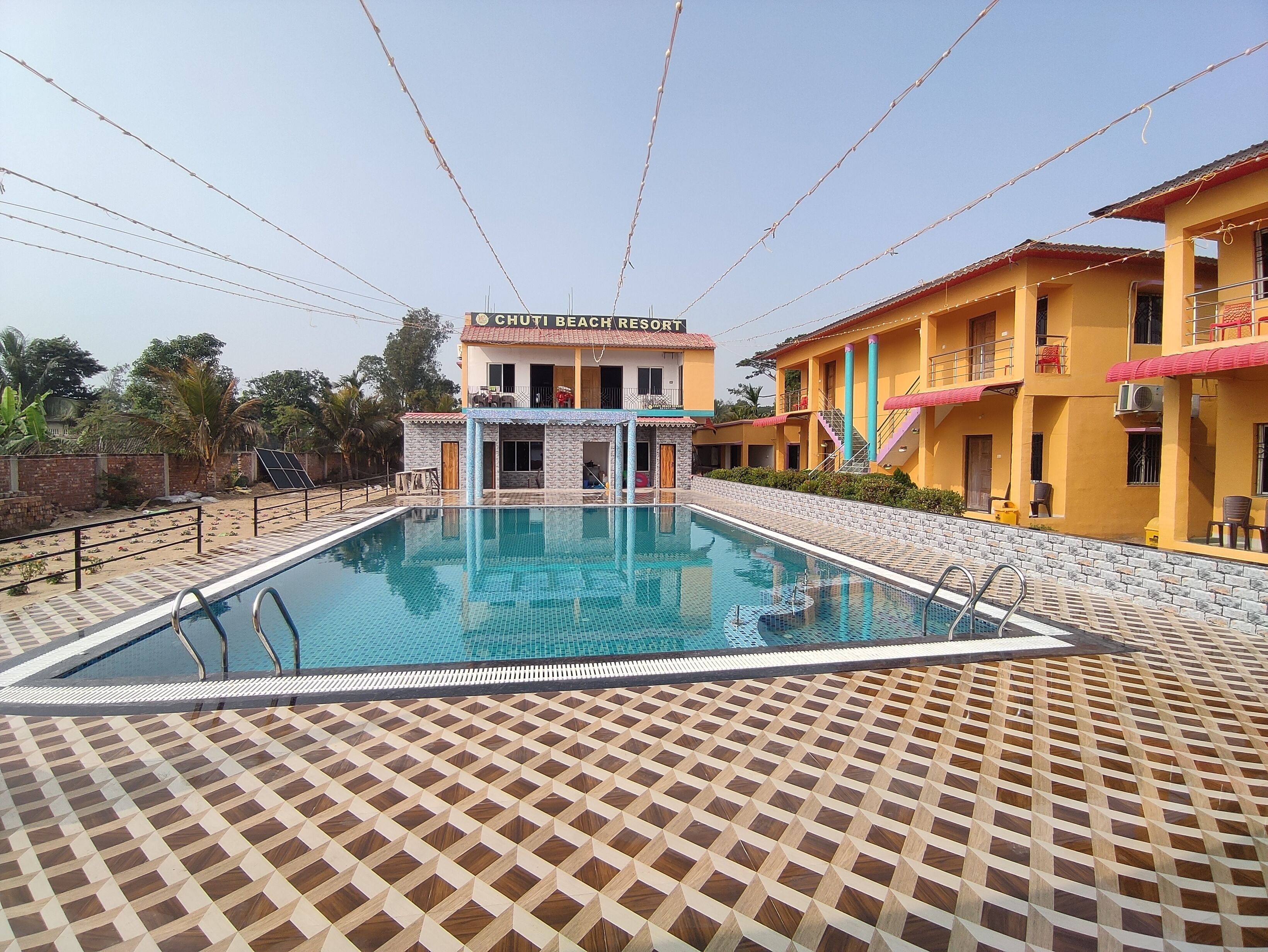 A swimming pool with a tiled deck, a building labeled 'Chuti Beach Resort', and a clear sky.