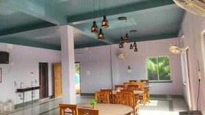A spacious dining area with multiple wooden tables and chairs, ceiling fans, and hanging pendant lights. - CHUTI BEACH REOSORT (Mandarmani)