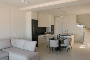 Una cuina moderna amb armaris blancs, un refrigerador negre i una zona de menjador amb taula i cadires.