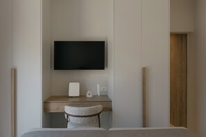 Un dormitori amb un llit, un escriptori amb cadira, una televisió i una estant penjada a la paret.