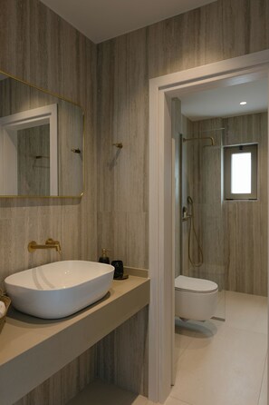 A modern bathroom with a large white sink, a gold faucet, a mirror with a gold frame, and a shower area with a glass door.