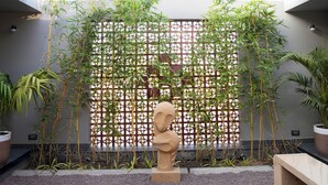 A modern indoor garden with a bamboo fence, a sculpture, and a bench. - Kshitij Villa (Bhuj)