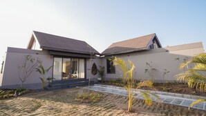 A modern house with a sloped roof, a covered porch, and a landscaped garden with palm trees. - Kshitij Villa (Bhuj)