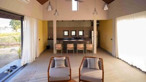A spacious living area with two armchairs, a kitchen with a bar, and large windows. - Kshitij Villa (Bhuj)