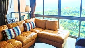 A corner sofa with striped pillows, a lamp, and a view of greenery through large windows. - The Unixx South Pattaya (Pattaya)