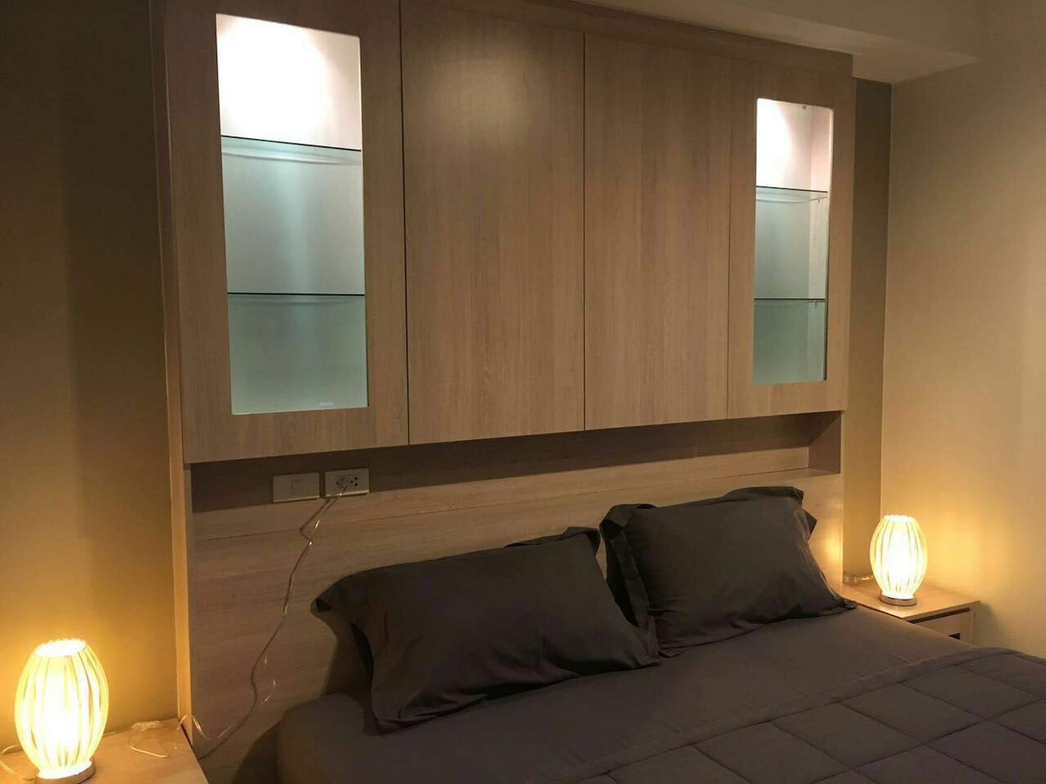 Une chambre à coucher moderne avec une tête de lit en bois, deux lampes de chevet et un lit avec une literie aux couleurs sombres.