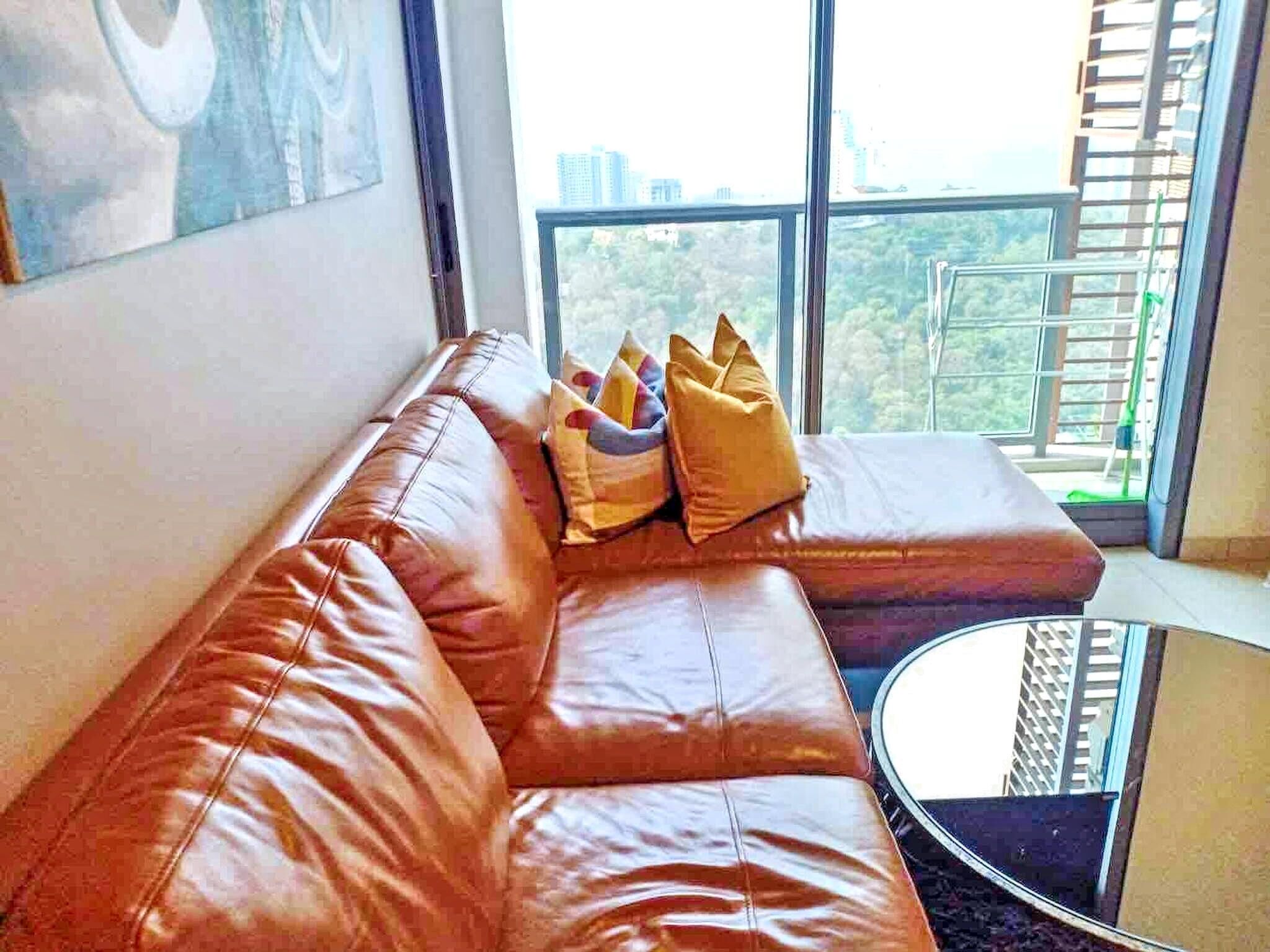 A modern living room with a leather sofa, a round glass coffee table, and a large window with a city view.