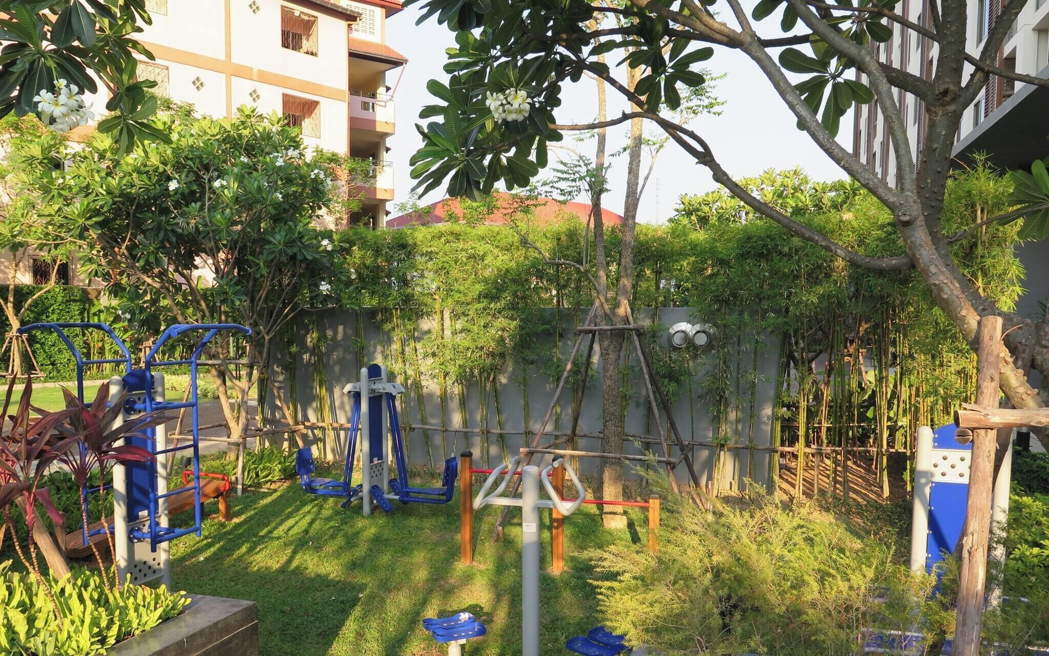 A playground with exercise equipment, surrounded by greenery and residential buildings.