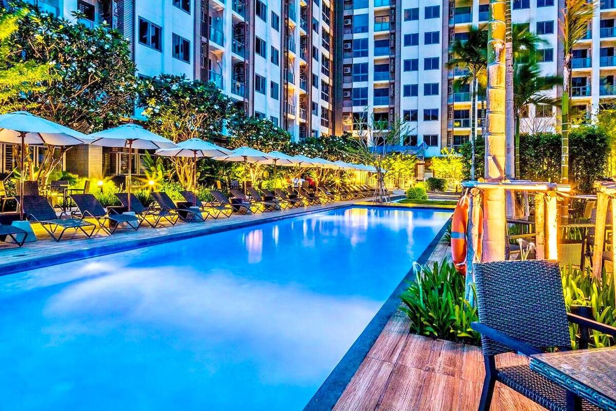 A swimming pool with lounge chairs and umbrellas, surrounded by high-rise buildings and greenery.