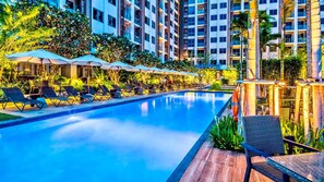 Ein Pool mit Liegestühlen und Sonnenschirmen, umgeben von Hochhäusern und Grünflächen.