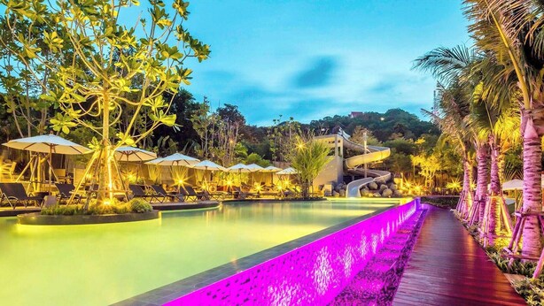 A pool area with lounge chairs and umbrellas, a water slide, and a wooden walkway. - The Unixx South Pattaya (Pattaya)