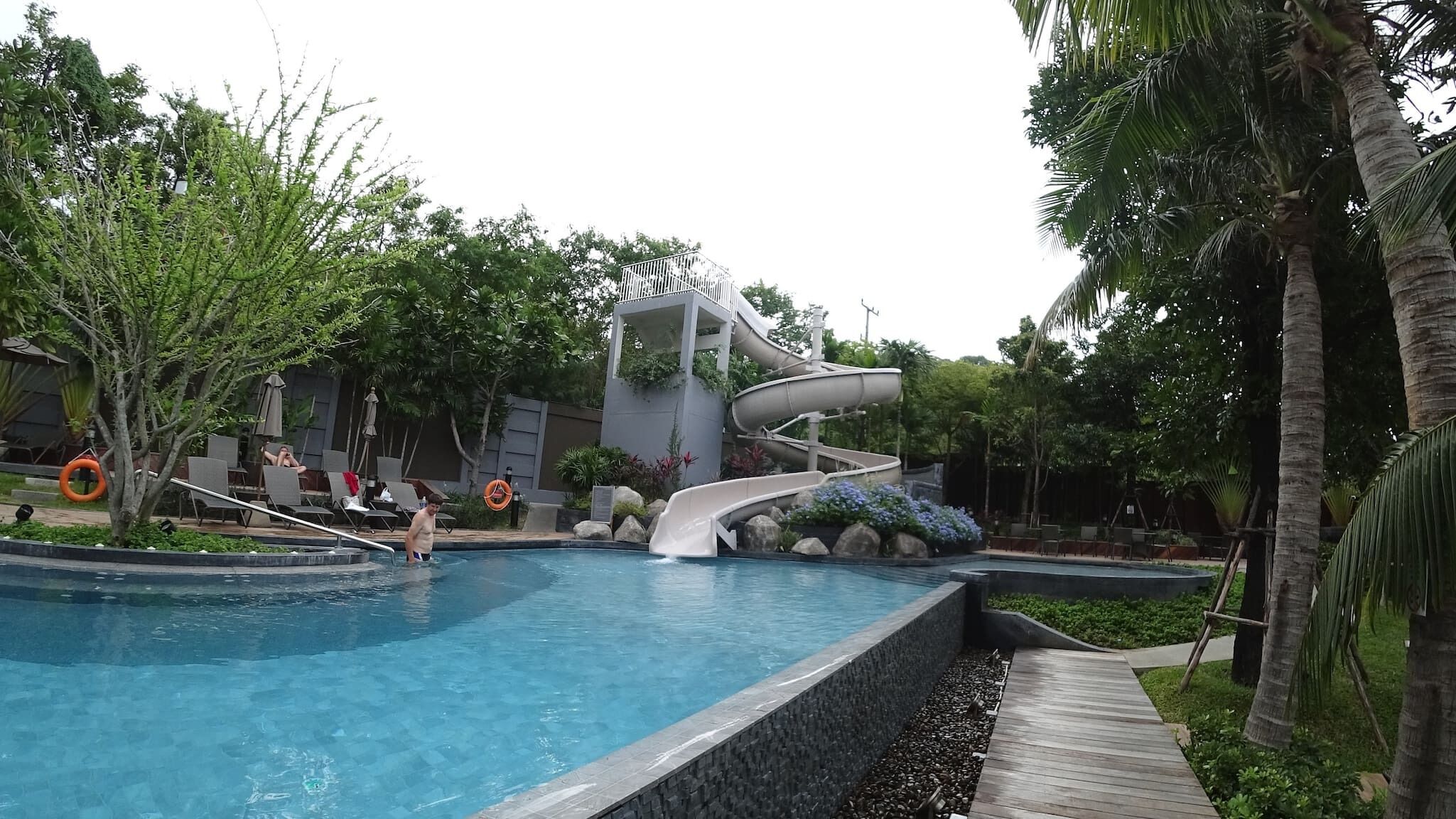 A swimming pool with a water slide, lounge chairs, and palm trees.
