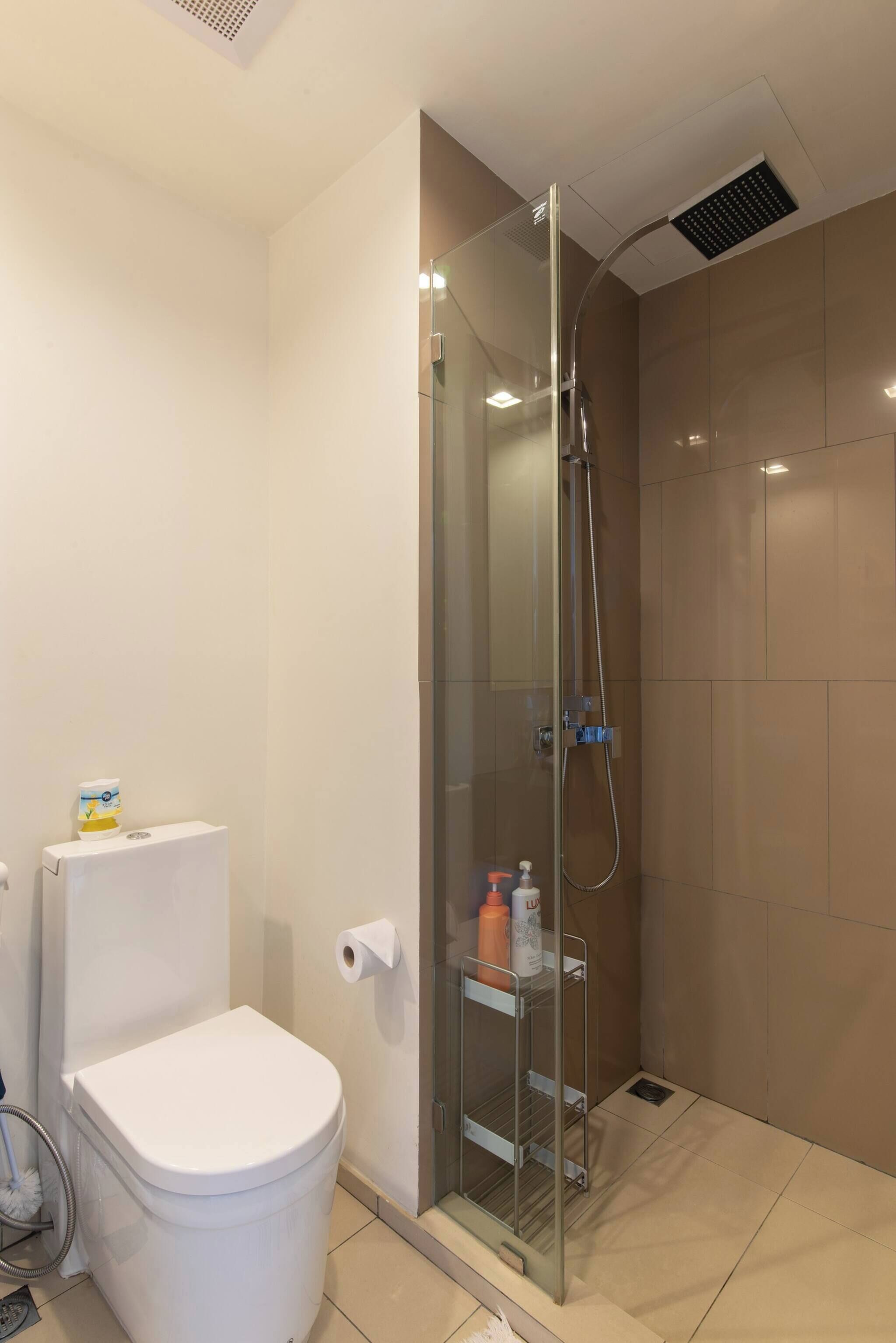 A modern bathroom with a glass-enclosed shower, a toilet, and a shelf with toiletries.