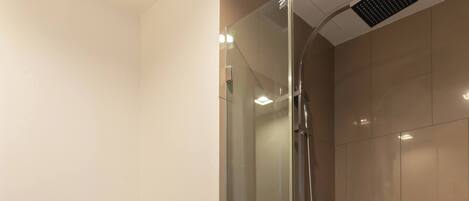 A modern bathroom with a glass-enclosed shower, a toilet, and a shelf with toiletries.