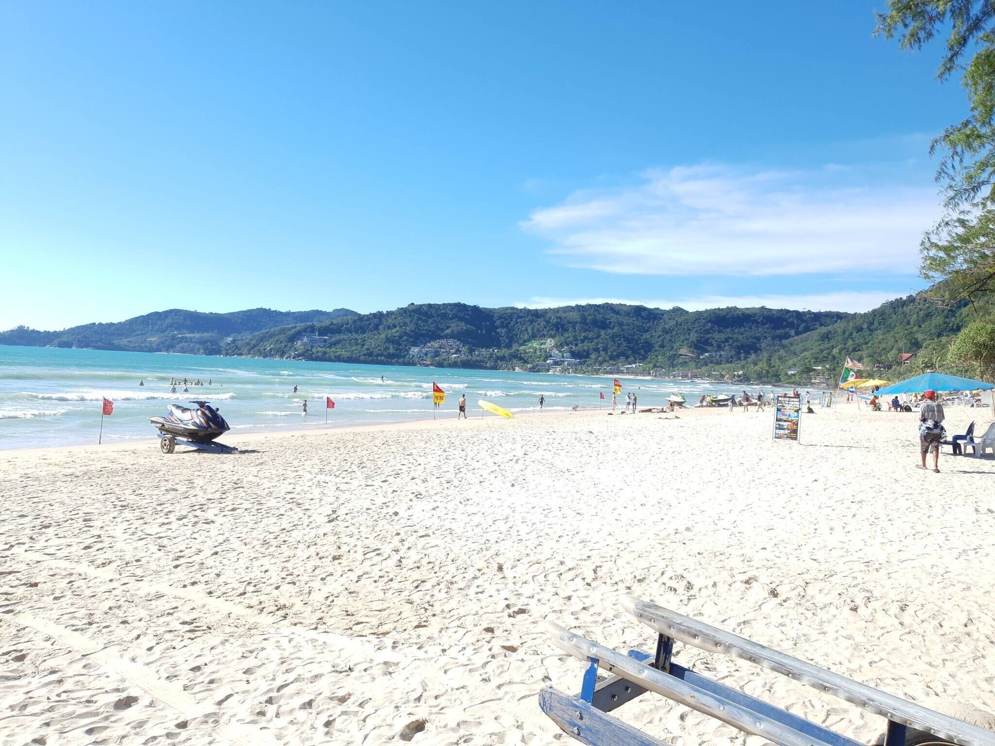 A sandy beach with a jet ski, beach umbrellas, and a lifeguard flag.