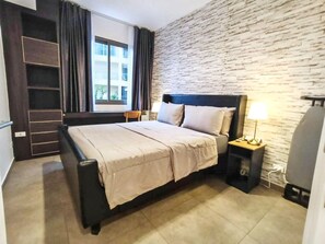 Ein Hotelzimmer mit einem Bett, einem Nachttisch, einer Lampe, einem Sessel, einem Kleiderschrank und einem Fenster mit Vorhängen.
