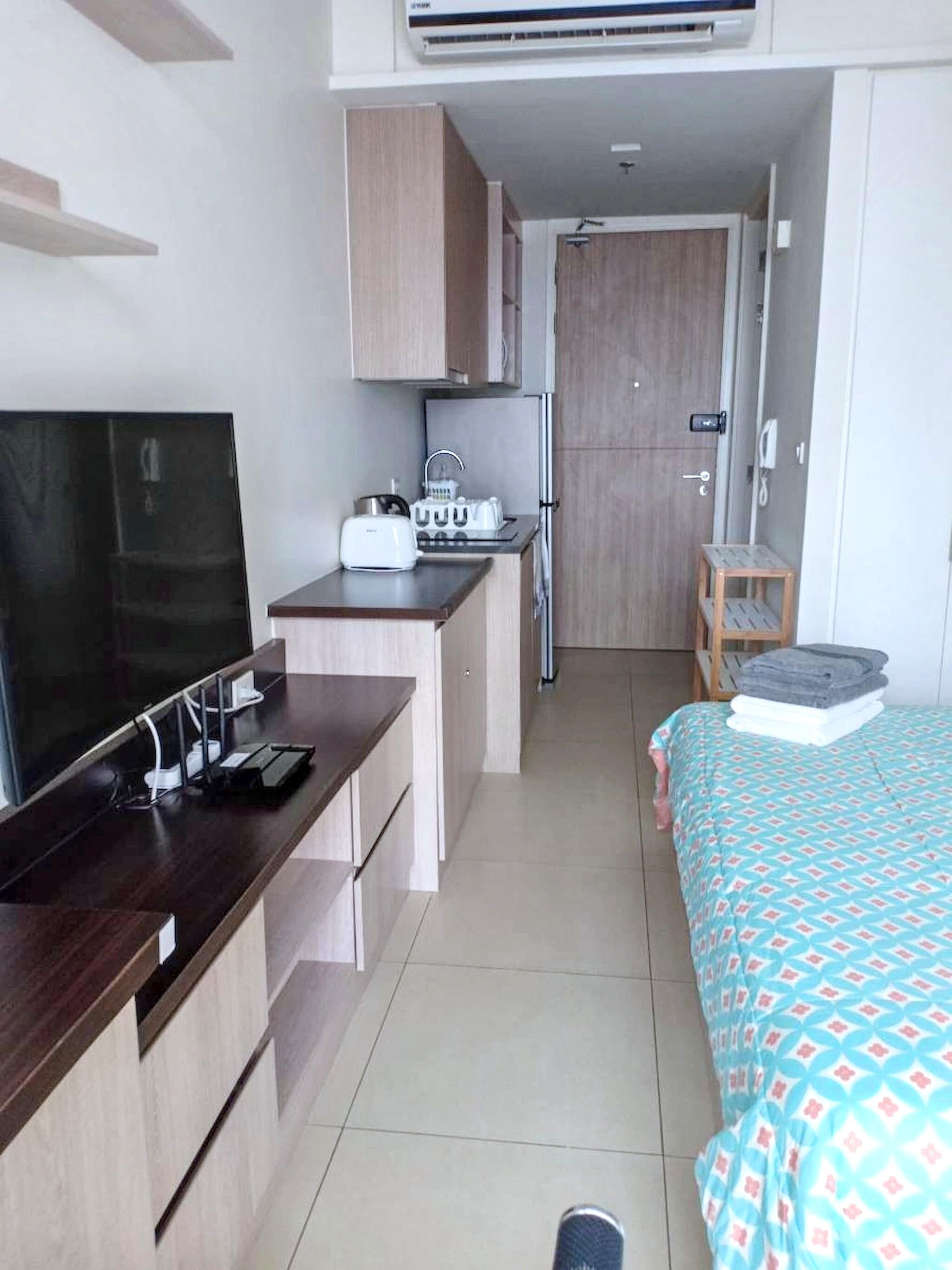 A compact hotel room with a kitchenette, a bed with patterned bedding, a TV, and a small table.