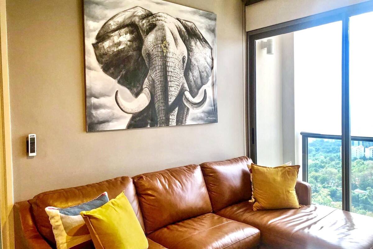 A brown leather sofa with yellow cushions and a large elephant artwork on the wall.