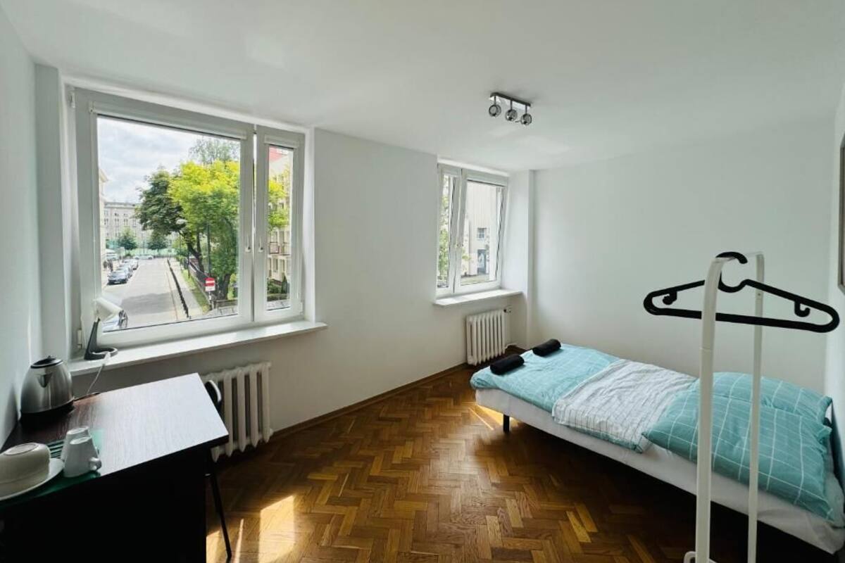 A room with a bed, a table with a kettle, and a radiator.