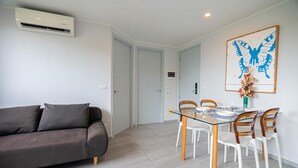 Un salon moderne avec un canapé gris, une table à manger en verre et des chaises en bois, ainsi qu’un tableau représentant un papillon accroché au mur.