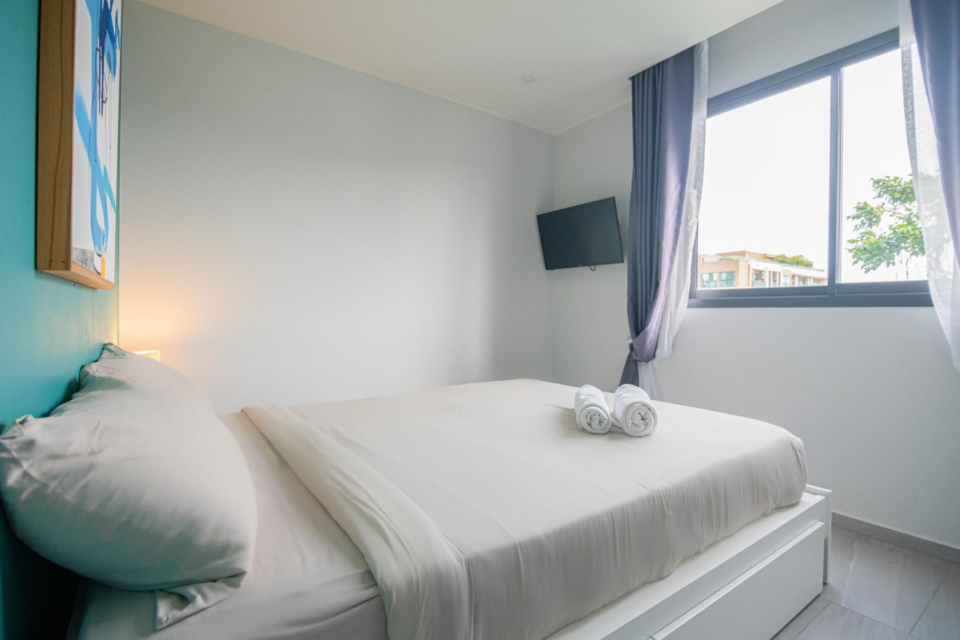Une chambre à coucher avec un lit, un téléviseur fixé au mur et une fenêtre avec des rideaux.