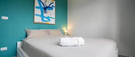A bedroom with a bed, a wall-mounted abstract painting, a bedside lamp, and a power outlet.