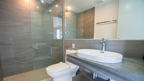 Une salle de bain moderne avec une douche à parois de verre, des toilettes blanches et un grand lavabo doté d’un plan de travail foncé.