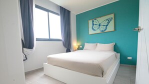Une chambre à coucher avec un lit, une fenêtre avec des rideaux, une œuvre d’art accrochée au mur et une lampe de chevet.
