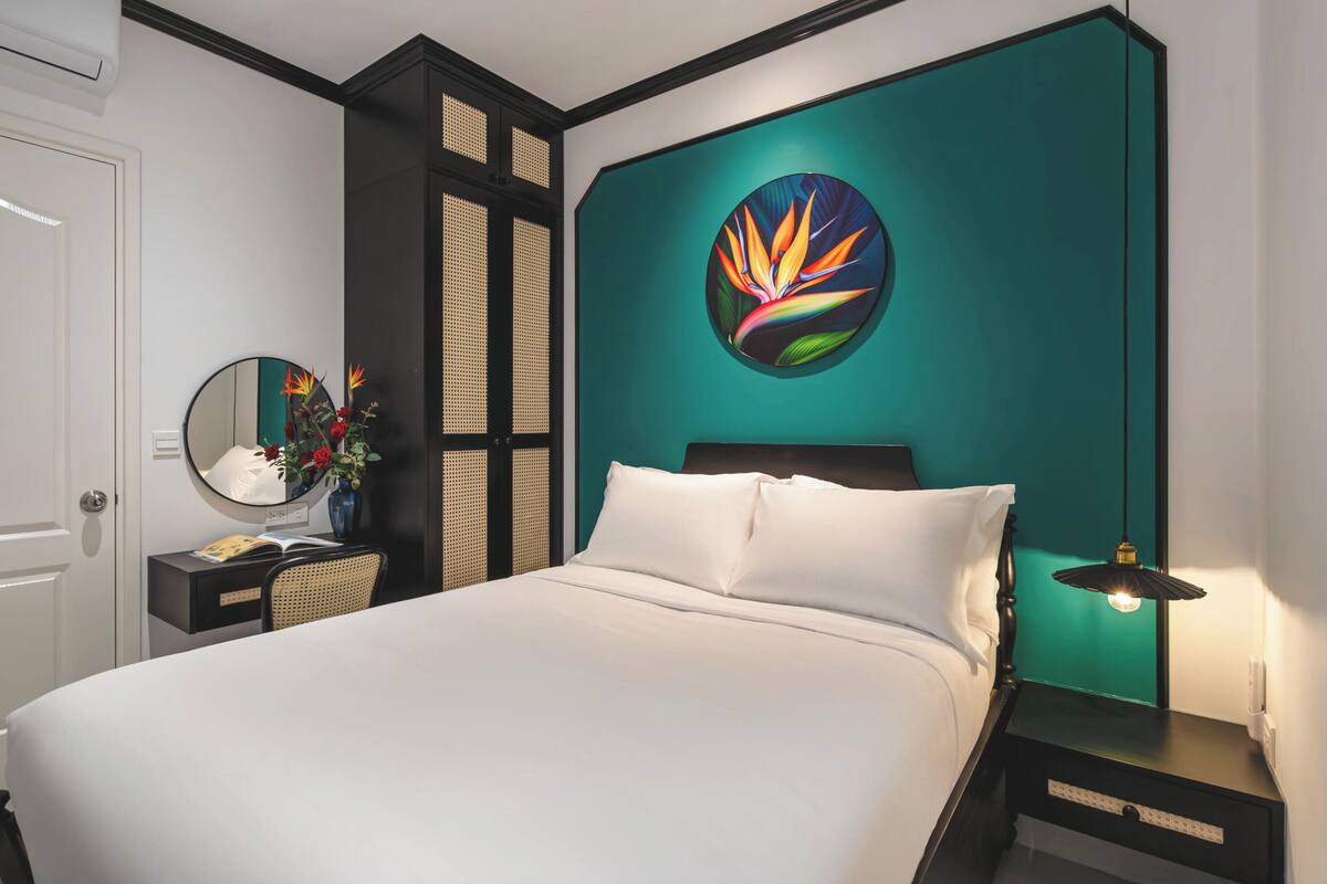 A bedroom with a bed, a bedside table with a lamp, a mirror, and a wall-mounted artwork.
