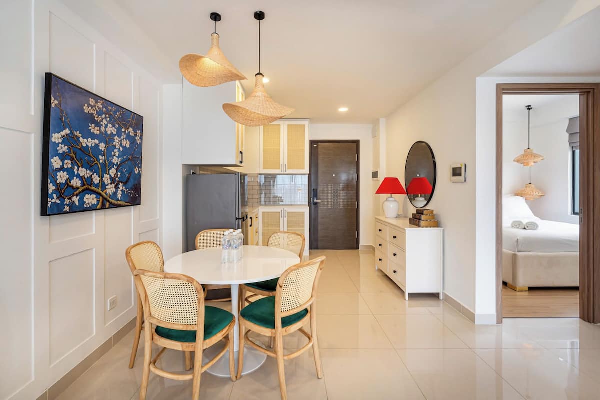 A modern kitchen with white cabinets, a dining table with wicker chairs, and pendant lighting.