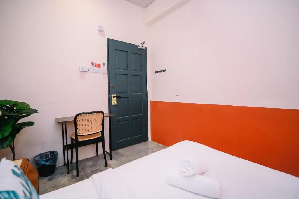 A small hotel room with a bed, a desk, a chair, and a door.