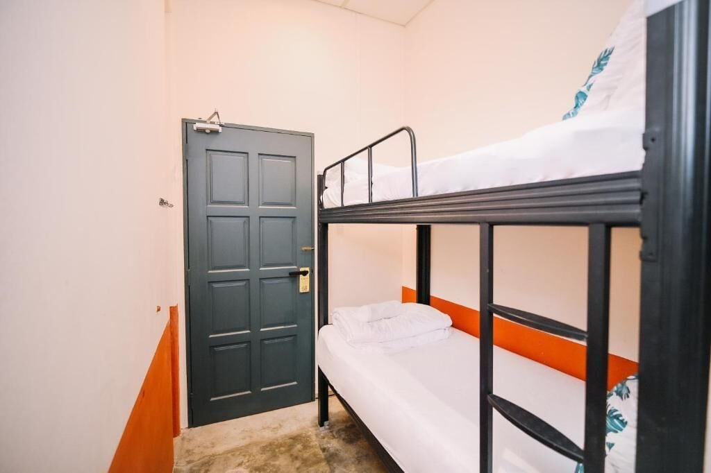 A small, single-bedded room with a bunk bed, a door, and a carpeted floor.