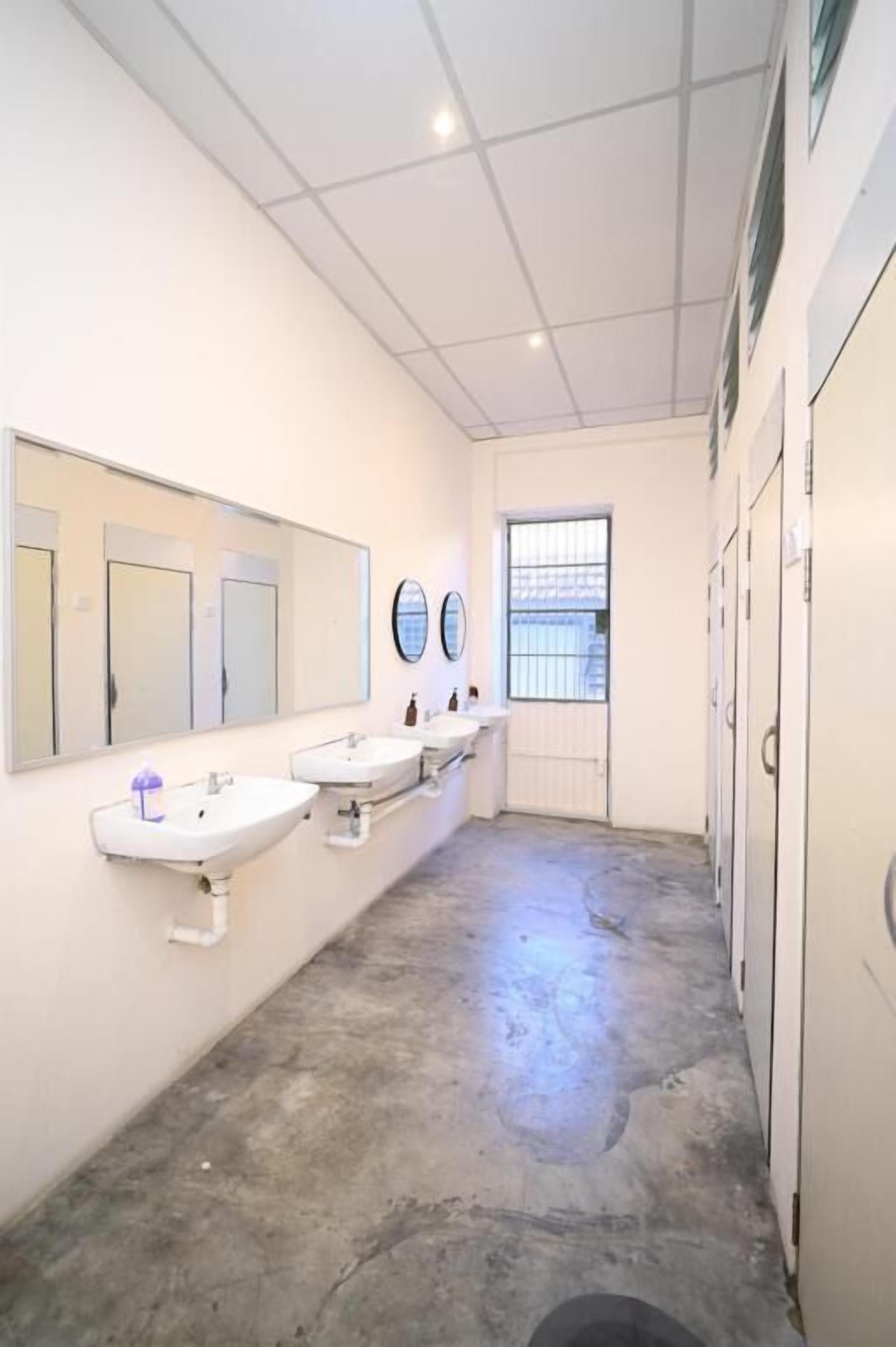 A restroom with three sinks, a large mirror, and a window with bars.