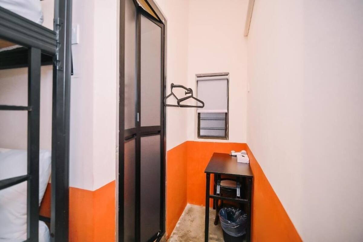 Ein kleiner, kompakter Raum mit einem Etagenbett, einem Tisch mit Stuhl, einer Mülleim darüber hinaus einen Kleiderhaken.