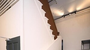 A staircase with a wooden handrail and a dark door at the bottom. - Swing & Pillows @ 75 Chulia St, Georgetown Penang (George Town)