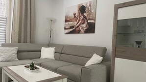 Un salon moderne avec un canapé gris, des coussins blancs, une table basse blanche ornée d’une plante et un tableau accroché au mur.
