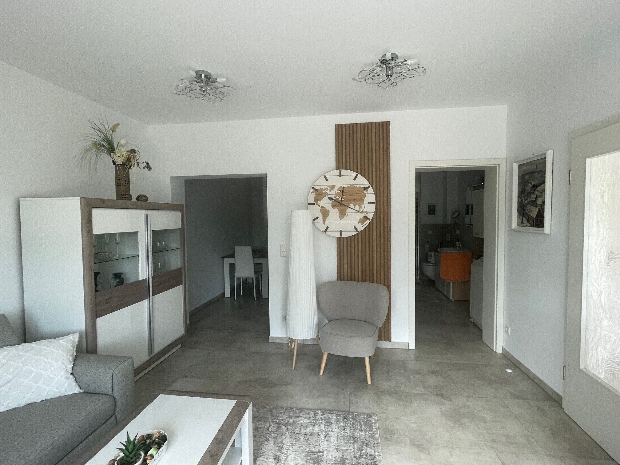 A modern living room with a sofa, a coffee table, a world map clock, and a dining area with a table and chairs.