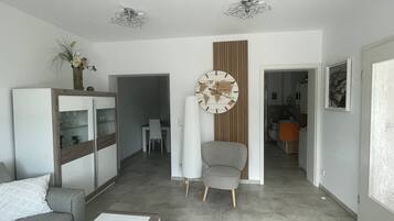 A modern living room with a sofa, a coffee table, a world map clock, and a dining area with a table and chairs.