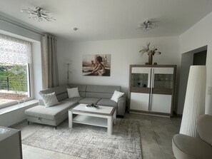 A modern living room with a grey sofa, a white coffee table, a cabinet with glass doors, and a painting on the wall.