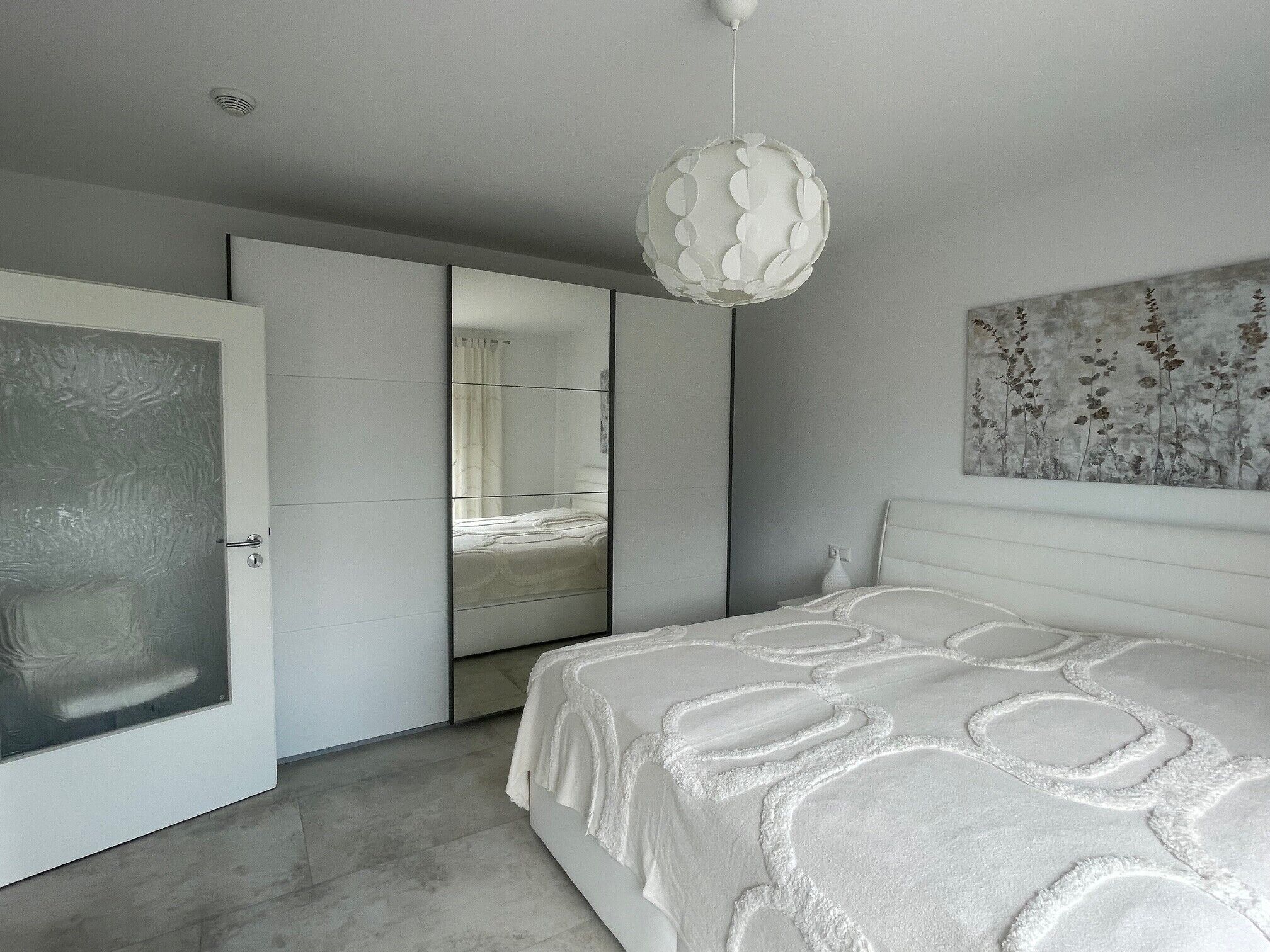 A modern bedroom with a large bed, a wardrobe, a mirror, and a pendant light.