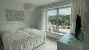 Une chambre à coucher avec un lit, une télévision, une fenêtre avec des rideaux et un tableau au mur.