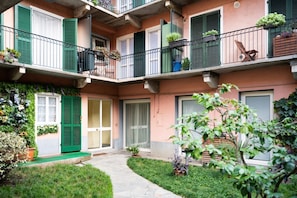 Un edificio de varios pisos con balcones, contraventanas verdes y macetas con plantas.