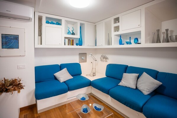 Una sala de estar moderna con dos sofás azules, una mesa de centro con objetos decorativos, y estanterías blancas con jarrones y libros azules.