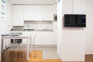 Une cuisine moderne avec des armoires blanches, un évier en acier inoxydable, une cuisinière et un téléviseur à écran plat fixé au mur.