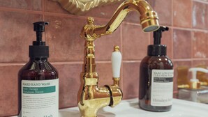 Un lavamanos de baño con dos botellas de jabón de manos y un grifo dorado.