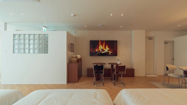 Habitación de hotel con dos camas, un escritorio con sillas, chimenea y un pequeño rincón de descanso con cojines.