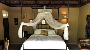 Un lit à baldaquin, une chaise en bois, un sol en pierre et une lampe fixée au mur.