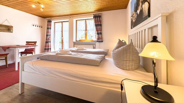 Et soveværelse med træloft, to senge med ternet sengetøj, et skrivebord og en lampe.